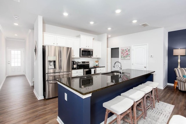 kitchen with a center island with sink, sink, dark hardwood / wood-style floors, appliances with stainless steel finishes, and white cabinetry