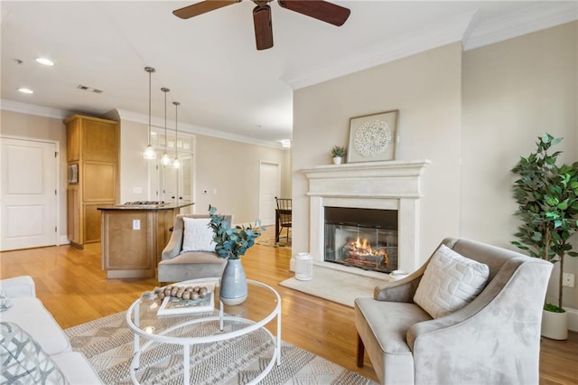 living room with light wood-type flooring, visible vents, ornamental molding, and a glass covered fireplace