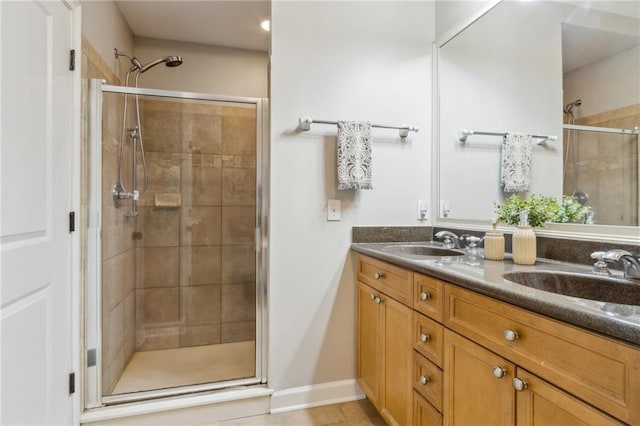 bathroom with baseboards, double vanity, a sink, and a shower stall