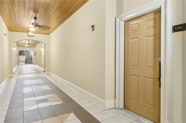 hall with arched walkways, light tile patterned floors, wooden ceiling, and baseboards