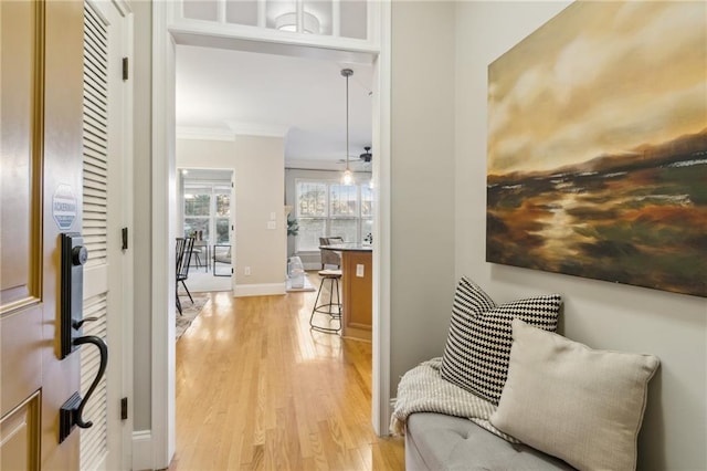 corridor with ornamental molding, light wood-style flooring, and baseboards