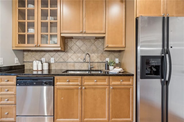 kitchen featuring decorative backsplash, glass insert cabinets, dark stone countertops, stainless steel appliances, and a sink