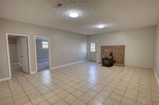 unfurnished living room with a textured ceiling, light tile patterned floors, and a wood stove