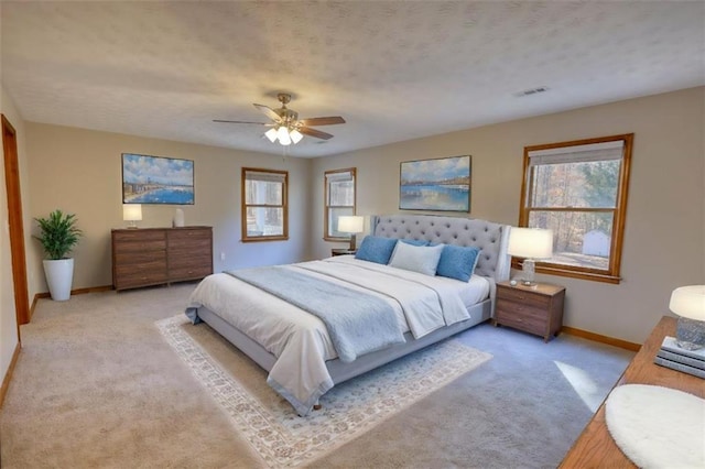 bedroom with ceiling fan, light colored carpet, and a textured ceiling