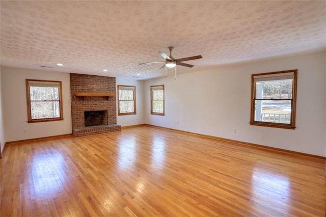 unfurnished living room featuring a brick fireplace, plenty of natural light, light hardwood / wood-style flooring, and ceiling fan