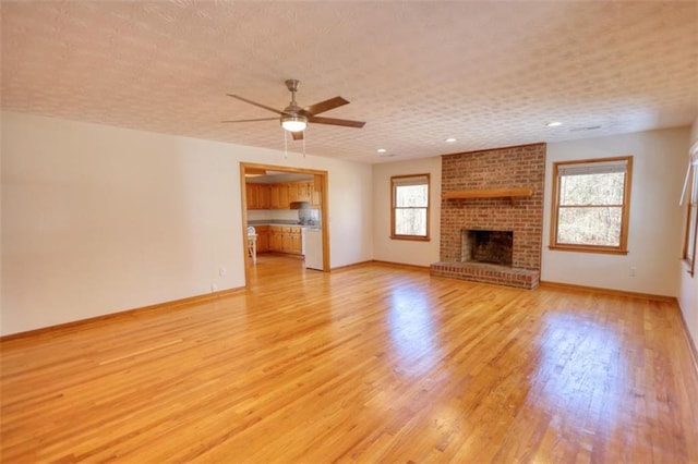 unfurnished living room featuring a textured ceiling, a brick fireplace, light hardwood / wood-style floors, and ceiling fan