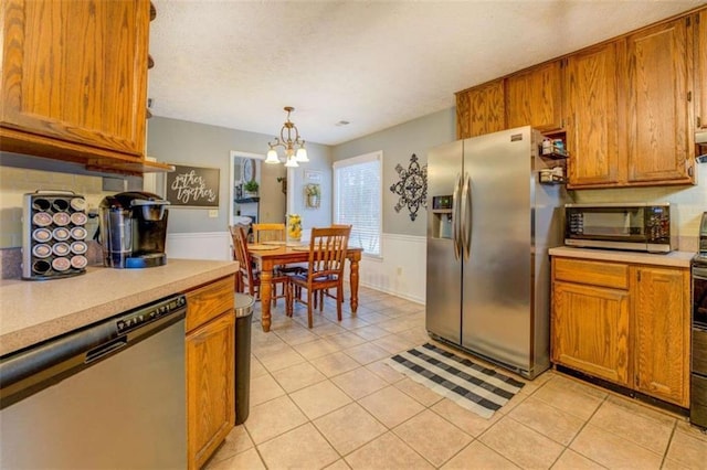 kitchen with light tile patterned flooring, an inviting chandelier, decorative light fixtures, appliances with stainless steel finishes, and decorative backsplash