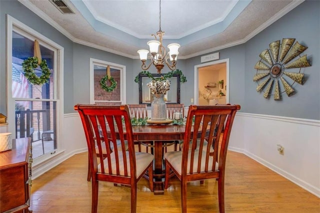 dining area featuring a raised ceiling, ornamental molding, a notable chandelier, and light wood-type flooring