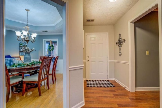 dining area with hardwood / wood-style floors, a notable chandelier, ornamental molding, a textured ceiling, and a raised ceiling