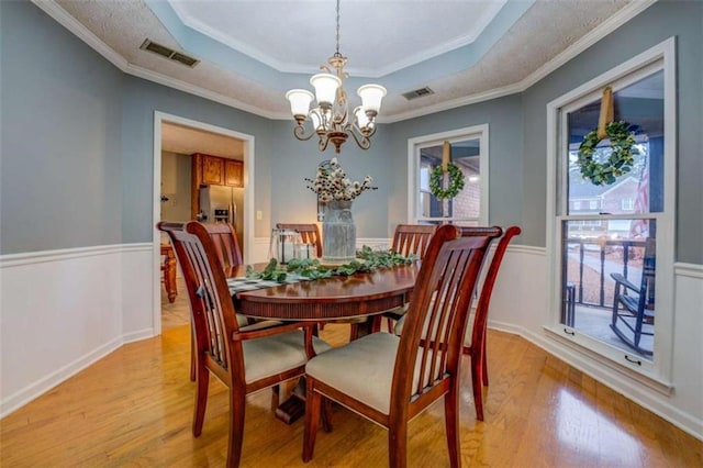 dining room with a notable chandelier, a tray ceiling, ornamental molding, and light hardwood / wood-style floors