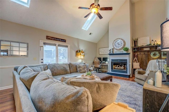 living room with hardwood / wood-style floors, a skylight, high vaulted ceiling, and ceiling fan