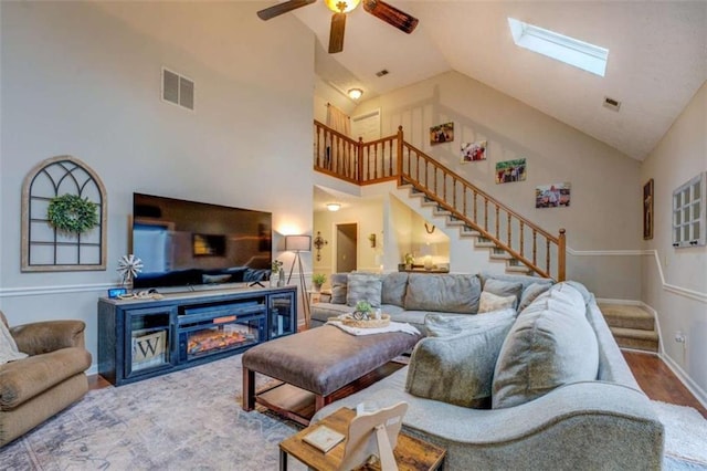 living room with high vaulted ceiling, hardwood / wood-style floors, ceiling fan, and a skylight