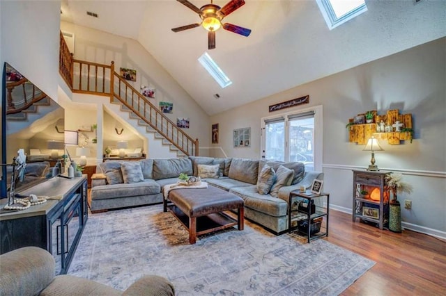 living room with ceiling fan, wood-type flooring, a skylight, and high vaulted ceiling