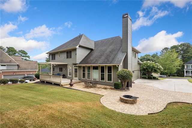 rear view of property with a wooden deck, a chimney, concrete driveway, a fire pit, and a lawn