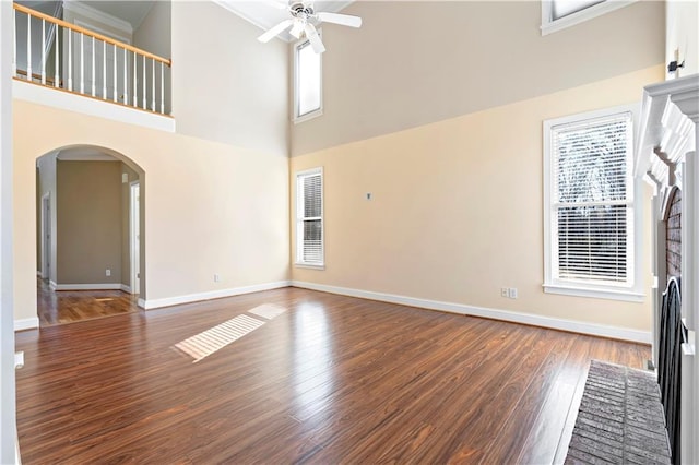 unfurnished living room with ceiling fan, a towering ceiling, dark wood-type flooring, and a wealth of natural light