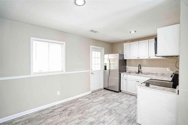 kitchen featuring stove, white cabinets, stainless steel refrigerator with ice dispenser, light stone countertops, and light wood-type flooring