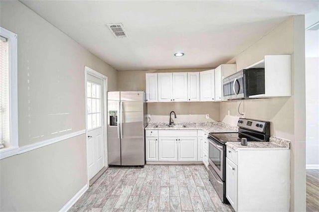 kitchen with light wood-type flooring, light stone counters, stainless steel appliances, sink, and white cabinets