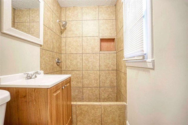 bathroom featuring tiled shower, vanity, a textured ceiling, and toilet