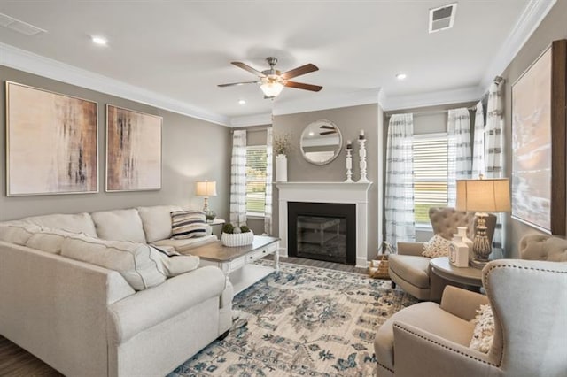 living room featuring crown molding, a ceiling fan, a glass covered fireplace, recessed lighting, and wood finished floors