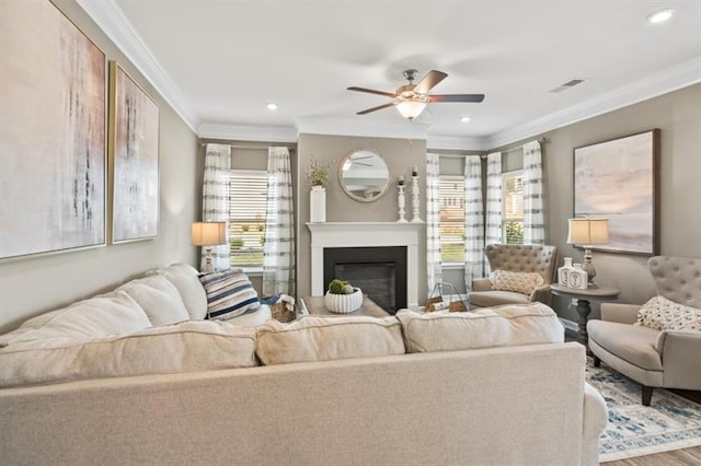 living room with ornamental molding, a ceiling fan, a glass covered fireplace, recessed lighting, and wood finished floors
