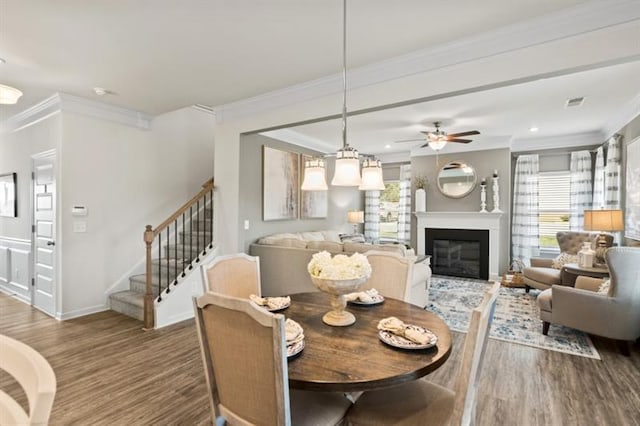 dining area featuring wood finished floors, crown molding, ceiling fan, baseboards, and stairway