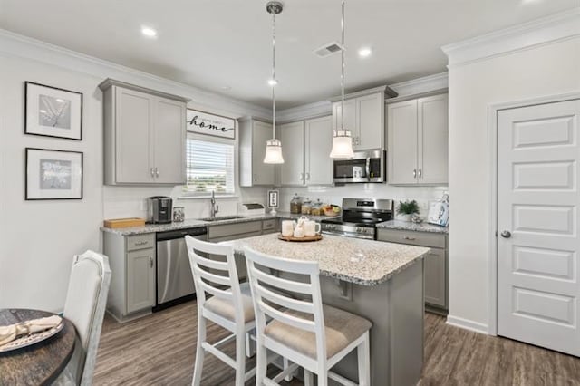 kitchen featuring appliances with stainless steel finishes, gray cabinets, a sink, a center island, and ornamental molding