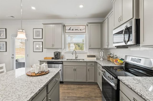 kitchen with appliances with stainless steel finishes, a sink, gray cabinetry, ornamental molding, and dark wood finished floors