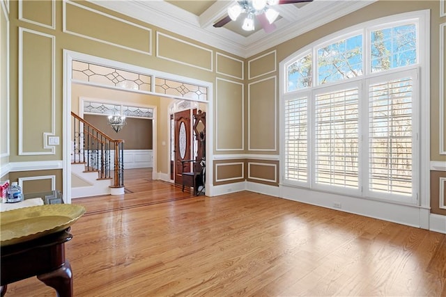 foyer featuring coffered ceiling, wood finished floors, crown molding, a decorative wall, and stairs