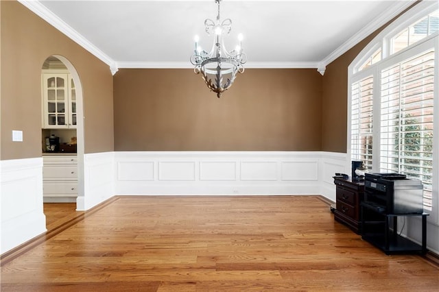 dining room featuring crown molding, a notable chandelier, light wood finished floors, and wainscoting