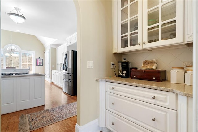 kitchen featuring backsplash, glass insert cabinets, vaulted ceiling, stainless steel refrigerator with ice dispenser, and arched walkways