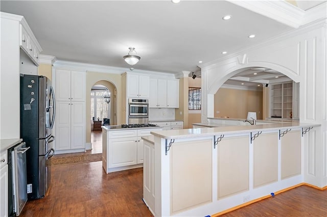 kitchen featuring dark wood finished floors, a peninsula, arched walkways, stainless steel appliances, and white cabinets