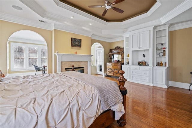 bedroom featuring visible vents, a fireplace, a raised ceiling, and wood finished floors