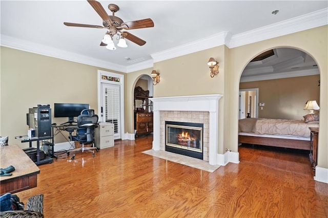 office featuring arched walkways, a tiled fireplace, crown molding, and wood finished floors