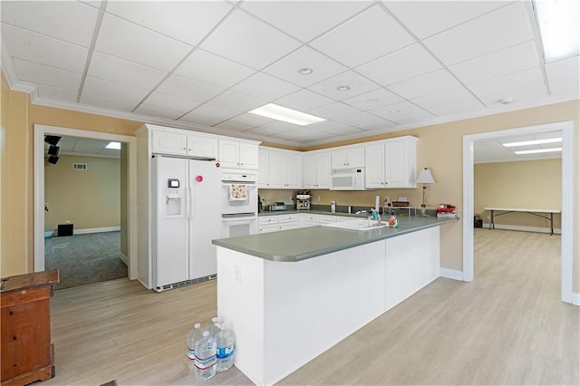 kitchen with light wood finished floors, a peninsula, white appliances, white cabinetry, and a sink