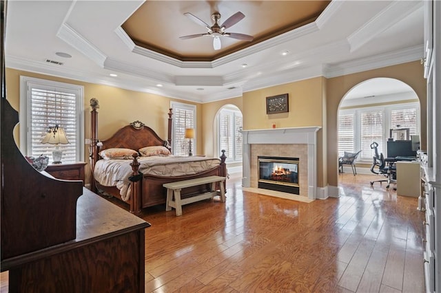 bedroom with light wood-type flooring, visible vents, ornamental molding, a tiled fireplace, and a tray ceiling