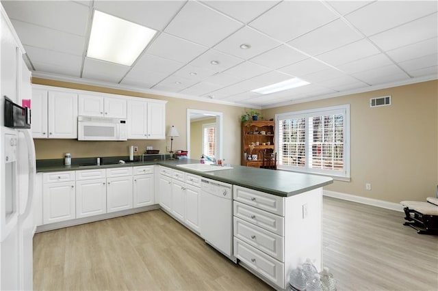 kitchen featuring a sink, dark countertops, white appliances, light wood-style floors, and a peninsula