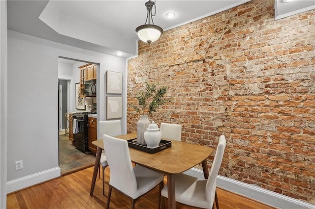 dining area with brick wall and light hardwood / wood-style floors