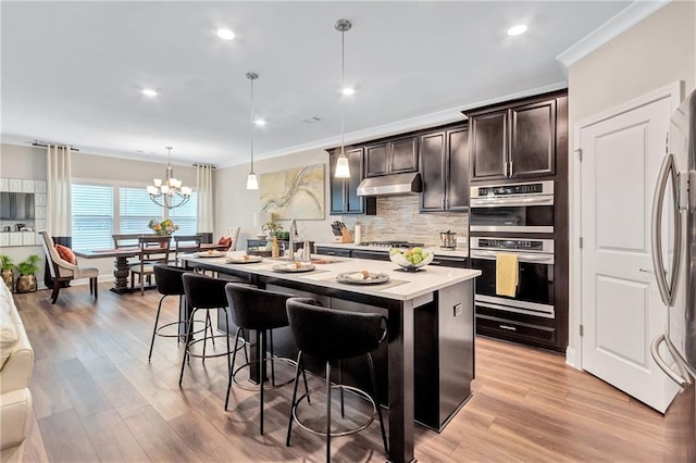 kitchen featuring appliances with stainless steel finishes, dark brown cabinets, a kitchen breakfast bar, a center island with sink, and decorative light fixtures