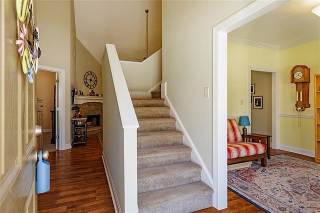 staircase with a stone fireplace, crown molding, wood finished floors, and baseboards