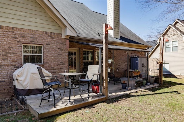 rear view of property featuring brick siding, a shingled roof, a chimney, a yard, and a deck