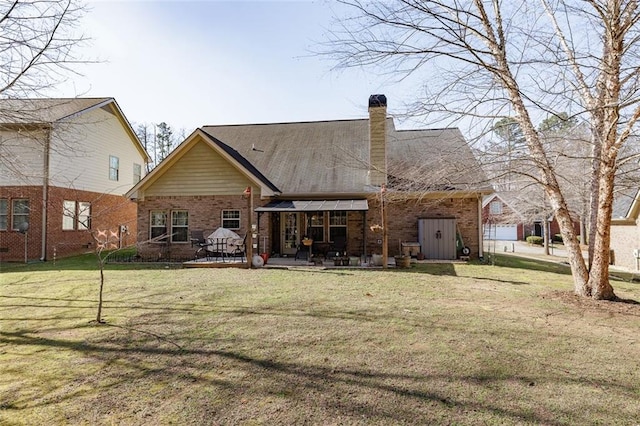 back of house featuring a patio, a yard, brick siding, and a chimney