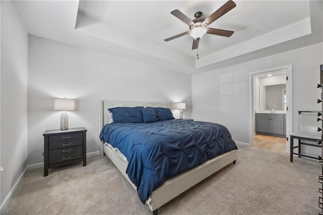 bedroom with baseboards, a tray ceiling, ensuite bath, and light colored carpet