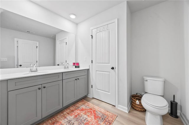 full bath featuring double vanity, a sink, toilet, and wood finished floors