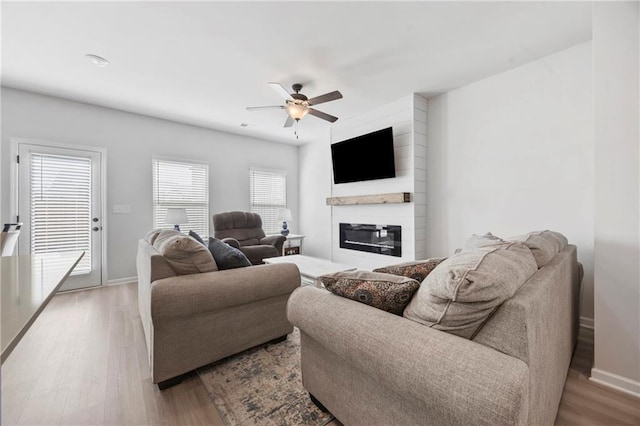 living room featuring a large fireplace, ceiling fan, baseboards, and wood finished floors