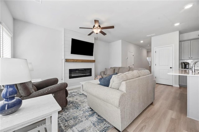 living area featuring light wood-style flooring, a fireplace, ceiling fan, and recessed lighting