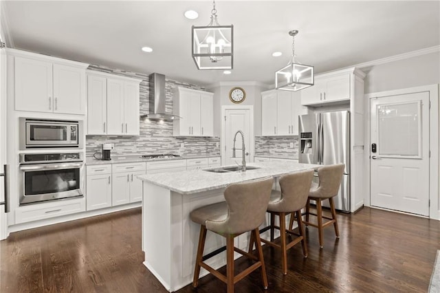 kitchen with wall chimney range hood, appliances with stainless steel finishes, crown molding, and a sink