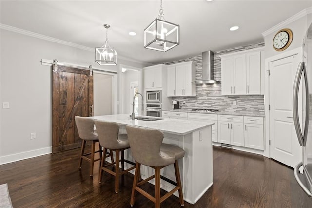 kitchen featuring appliances with stainless steel finishes, a sink, wall chimney exhaust hood, tasteful backsplash, and an island with sink