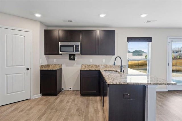 kitchen featuring light stone countertops, sink, dark brown cabinets, and light wood-type flooring