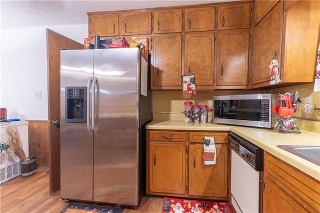265 Forest Lake Dr, Covington, GA 30016 - kitchen featuring appliances with stainless steel finishes, brown cabinetry, light countertops, light wood-style flooring, and a wainscoted wall