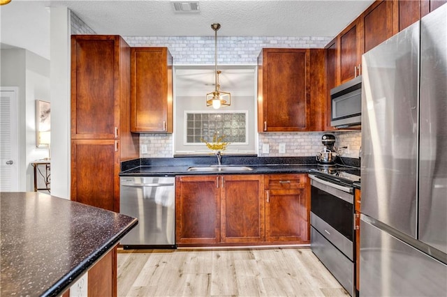 kitchen with pendant lighting, sink, appliances with stainless steel finishes, dark stone counters, and light wood-type flooring